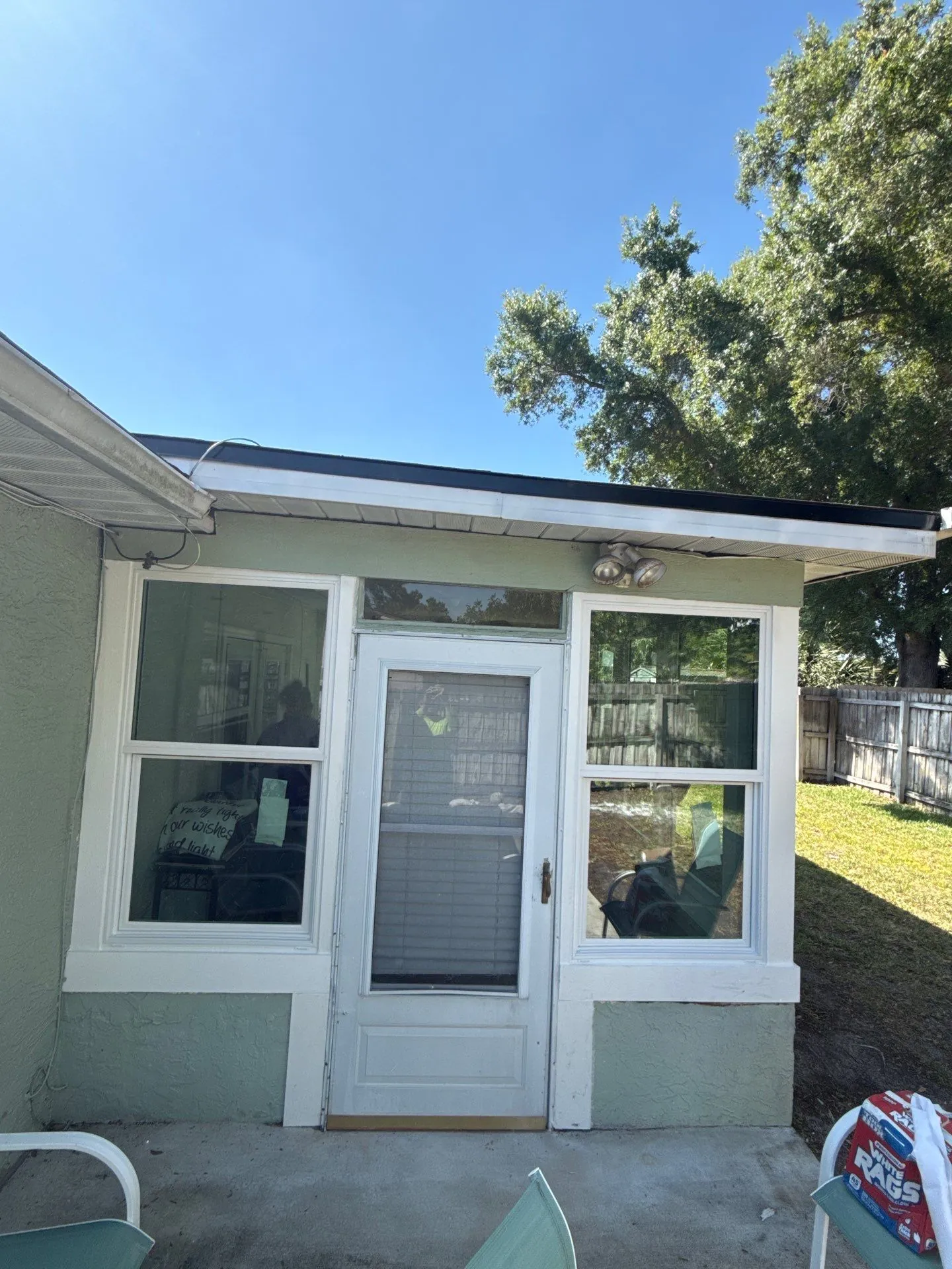 Rear entry door with a full-length glass panel flanked by two windows on a Florida home, with an open backyard, wood fence, and mature oak tree beyond the roofline