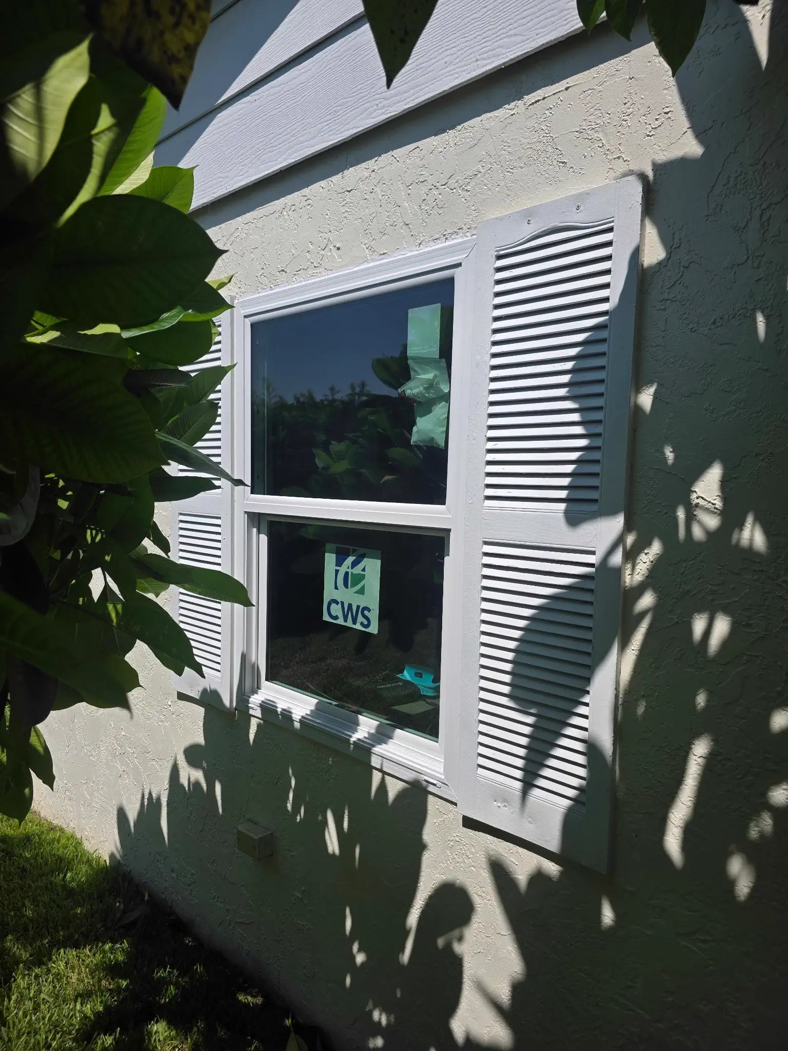 Exterior view of a light-colored home with a run of white-framed windows along the wall, seen from the yard on a bright day.