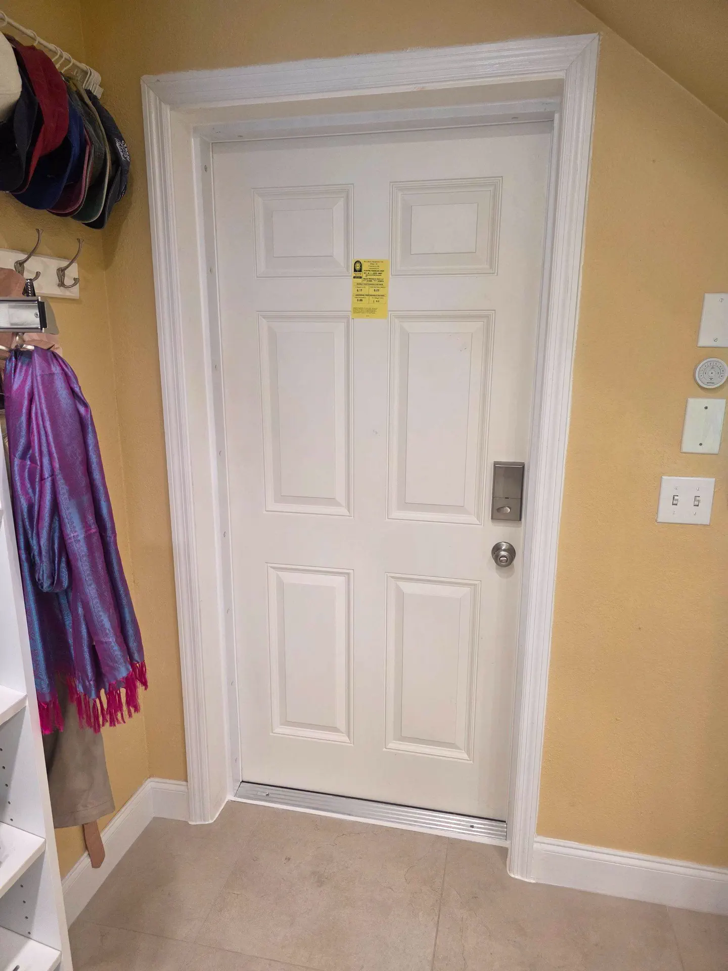 Interior view of a newly installed white six-panel entry door set in white trim, with the manufacturer's performance label still on the panel, a deadbolt and knob on the lock side, and a metal threshold along the bottom.
